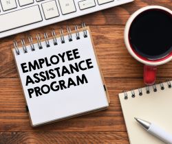 A desk with a laptop, coffee, and a notepad with employee assistance program written on it.