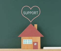 a cutout of a brown house in front of a chalk board. Above the house it has a heart with the word support inside.