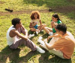 Group of four teenagers sitting in a circle on the grass outside talking