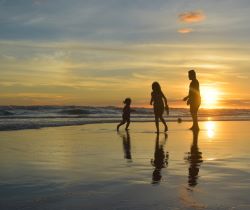 Two adults playing with a child on the beach during a sunset